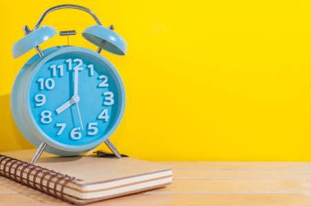 Blue analog alarm clock on a note book with yellow background.の写真素材