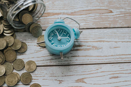 jar of coins with analog alarm clock on vintage wooden table.Financial and investment concept.の写真素材