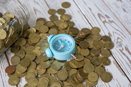 jar of coins with analog alarm clock on vintage wooden table.Financial and investment concept.
