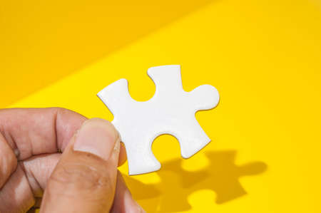 Man's hand holding a piece of white blank puzzle over yellow background.の写真素材