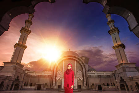 Beautiful Arab girl wearing hijab standing in front of Moswque during sunset.Muslim female at the mosque.の写真素材