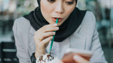 Beautiful young Muslim business woman using her smart phone at cafeteria.の写真素材