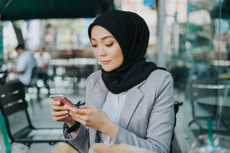 Beautiful young Muslim business woman using her smart phone at cafeteria.の写真素材