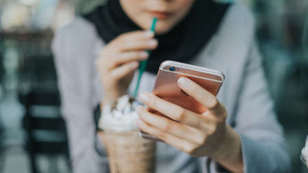 Beautiful young Muslim business woman using her smart phone at cafeteria.の写真素材