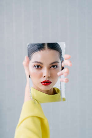 Beautiful girl holding a broken mirror with reflection of her beautiful face.Beauty and fashion shoot.Close up.の写真素材