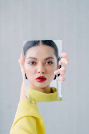 Beautiful girl holding a broken mirror with reflection of her beautiful face.Beauty and fashion shoot.Close up.の写真素材