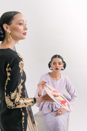 Beautiful girls wearing Baju Kurung and holding paint brush with blank white canvas isolate over white background.Modern female fashion fro Eid Ul Fitr celebration or formal event.Copy Space.の写真素材