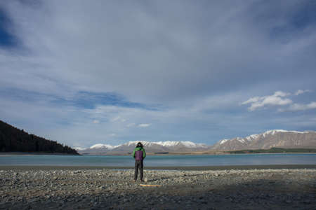 A man hiking by the lake shore with beatiful snow capped mountains in the background.View from behind.の写真素材