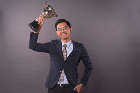 Happy young male intrepreneur or business man holding his gold trophy and celebrating his victory.Studio shot.の写真素材
