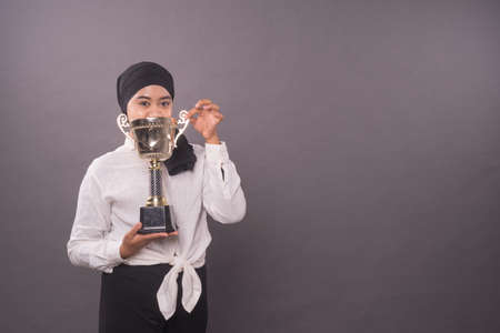 Happy young female entrepreneur or business woman holding her gold trophy and celebrating her victory.Studio shot.の写真素材