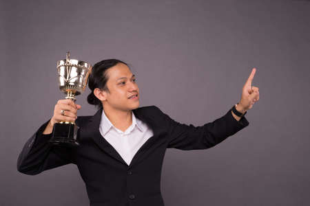 A young business man holding a gold trophy and celebrate his archivement.の写真素材