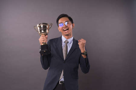 Happy young male intrepreneur or business man holding his gold trophy and celebrating his victory.Studio shot.の写真素材