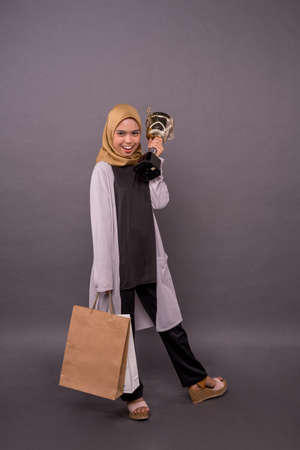 Clever Consumer concept.Happy malay girl holding shopping bags and Gold trophy.の写真素材