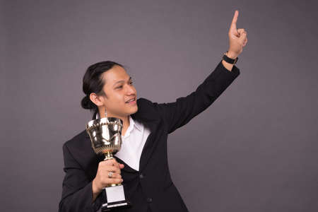 A young business man holding a gold trophy and celebrate his archivement.の写真素材