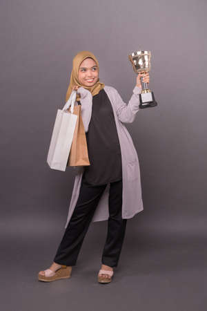 Clever Consumer concept.Happy malay girl holding shopping bags and Gold trophy.の写真素材