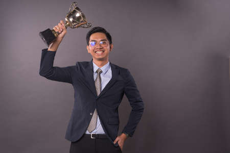 Happy young Asian male business man or student holding his gold trophy and celebrating his victory.Studio shot.の写真素材