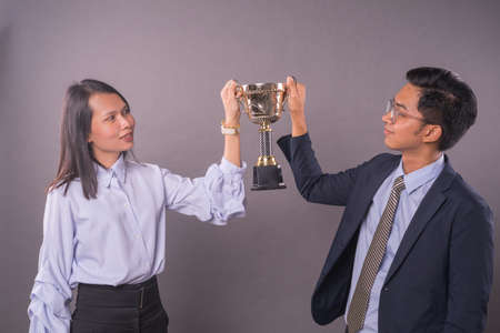 Successful team work.Businessman and woman holding a gold trophy.