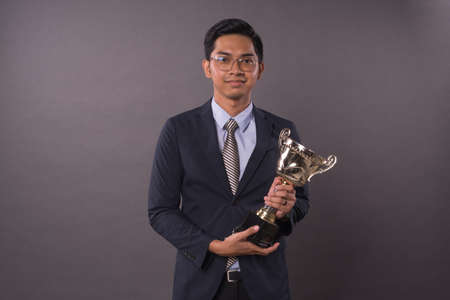 Happy young male entrepreneur or business man holding his gold trophy.Studio shot.の写真素材
