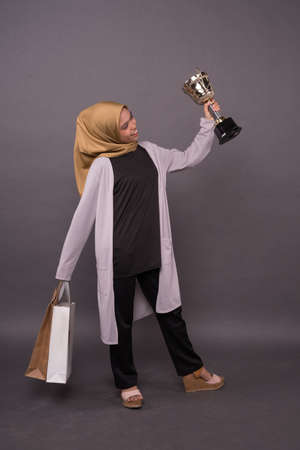 Clever Consumer concept.Happy malay girl holding shopping bags and Gold trophy.の写真素材