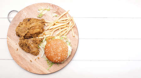 Fried chickens,cheese burger with fries on wooden chopping board isolated over white background.の写真素材