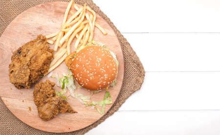 Fried chickens,cheese burger with fries on wooden chopping board isolated over white background.の写真素材