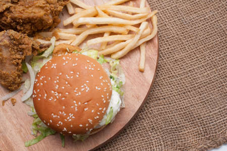 Fried chickens,cheese burger with fries on wooden chopping board with vintage canvas background.View from top.の写真素材