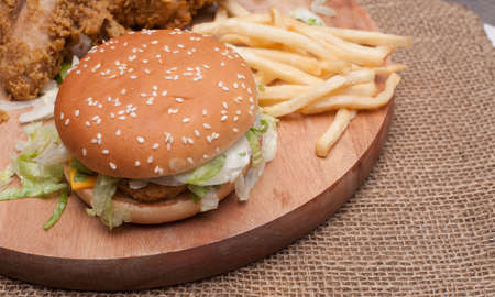 Fried chickens,cheese burger with fries on wooden chopping board with vintage canvas background.View from top.の写真素材