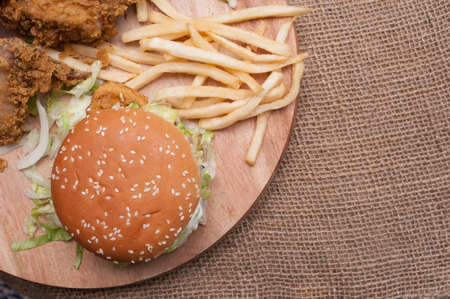 Fried chickens,cheese burger with fries on wooden chopping board with vintage canvas background.View from top.の写真素材