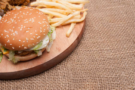 Fried chickens,cheese burger with fries on wooden chopping board with vintage canvas background.View from top.の写真素材