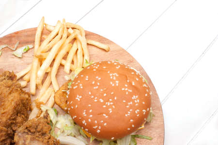 Fried chickens,cheese burger with fries on wooden chopping board isolated over white background.の写真素材