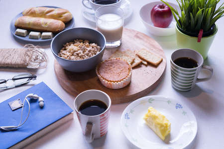 Top view of breakfast menu on white dining table.Coffee,milk, cereal, apple,cracker and bun on white table view from top.Food lay flat concept.の写真素材