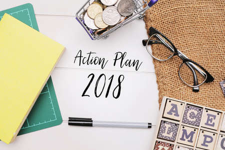 Books,pen and coins on white table written with text "Action Plan"の写真素材