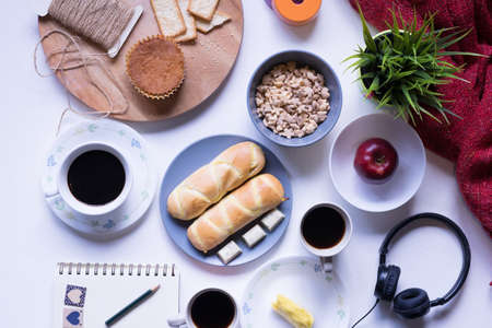 Top view of breakfast menu on white dining table.Coffee,milk, cereal, apple,cracker and bun on white table view from top.Food lay flat concept.の写真素材