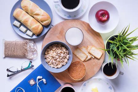Top view of breakfast menu on white dining table.Coffee,milk, cereal, apple,cracker and bun on white table view from top.Food lay flat concept.の写真素材