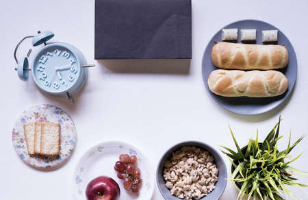 Top view of breakfast menu on white dining table.Coffee,milk, cereal, apple,cracker and bun on white table view from top.Food lay flat concept.の写真素材