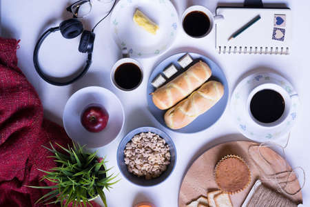 Top view of breakfast menu on white dining table.Coffee,milk, cereal, apple,cracker and bun on white table view from top.Food lay flat concept.の写真素材