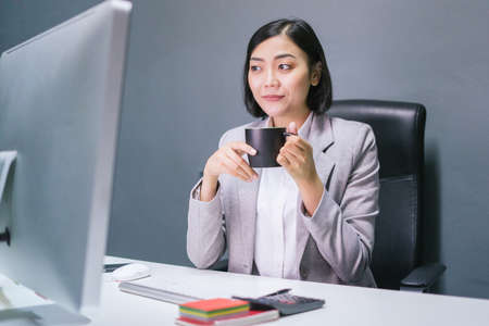 Happy asian female worker at having coffee at her office desk and smiling.の写真素材