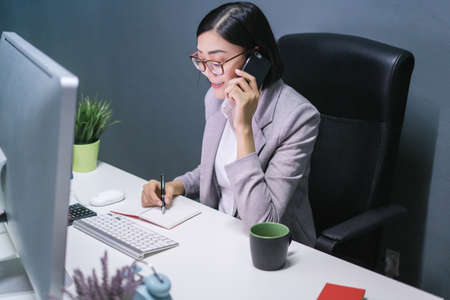 Happy chinese female worker at her office desk answering phone and smiling.Happy business woman.の写真素材