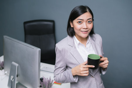 Happy female worker at her office desk holding cup and smiling.の写真素材