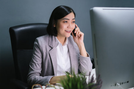 Happy female worker at her office desk using her smart phone and smiling.の写真素材