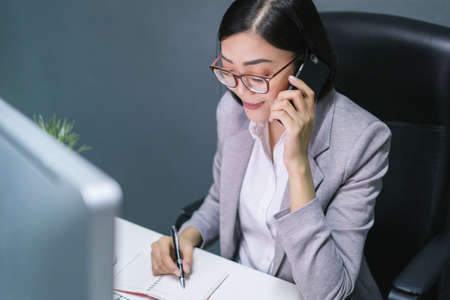 Happy chinese female worker at her office desk answering phone and smiling.Happy business woman.の写真素材