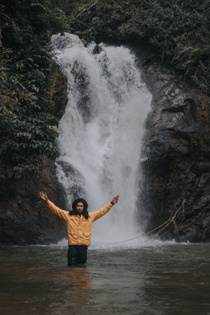 An asian male traveler enjoying the beauty of rainforest waterfall.A male explorer in the waterfall pool.Camping and hiking lifestyle.Into the wild.の写真素材