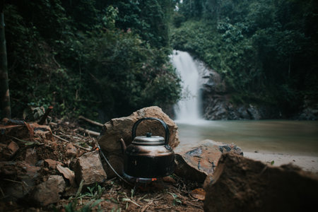Boiling water in the keetle using camping stove with waterfall in the background.の写真素材