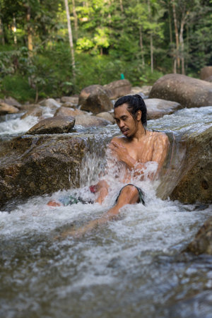 A male traveler enjoying the cold of rainforest stream during morning.Man shower in the waterfall pool.の写真素材