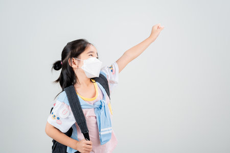 Asian little child girl carry a backpack wearing respirator mask to protect coronavirus outbreak and pointing hand to blank background, New virus Covid-19の写真素材