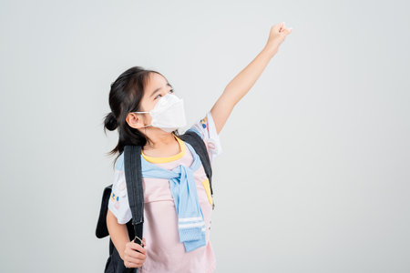 Asian little child girl carry a backpack wearing respirator mask to protect coronavirus outbreak and pointing hand to blank background, New virus Covid-19の写真素材
