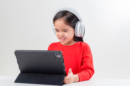 little girl asia cute put on headphones have video call distant class with teacher using laptop,  study online on computer, homeschooling conceptの写真素材