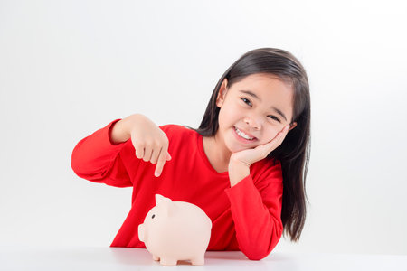 Little Asian girl saving money in a piggy bank, learning about saving, Kid save money for future education. Money, finances, insurance, and people conceptの写真素材