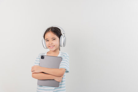 smiling little girl stiiting and holding a tablet with earphoneの写真素材