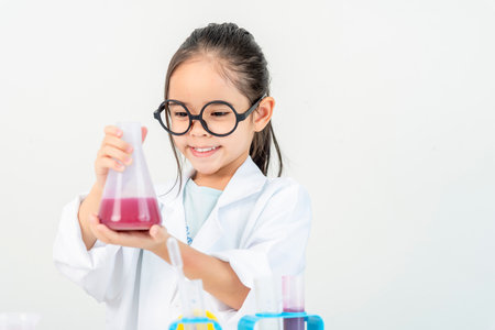 education, science and children concept girl in goggles with magnifier studying test tube with chemical at home laboratoryの写真素材